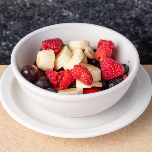 A white bowl filled with fresh fruit, including raspberries, banana slices, and blueberries.