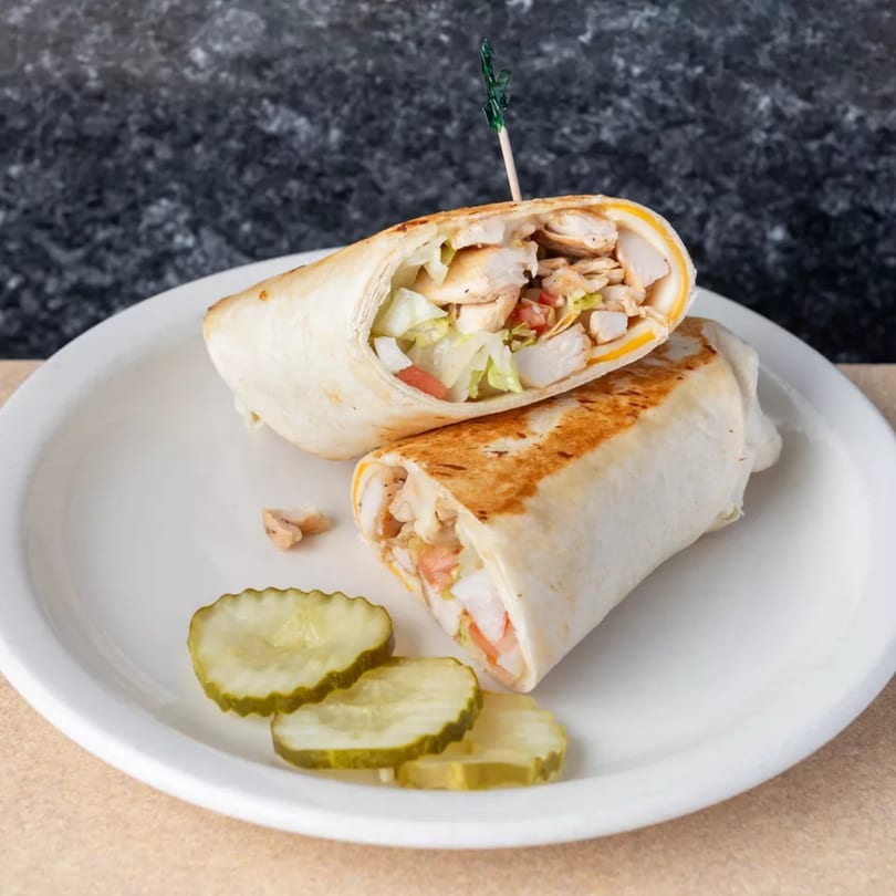 Two grilled chicken wraps with lettuce, tomato, and cheese, served with pickle slices on a white plate.