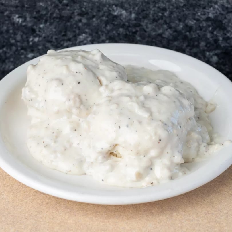 A white bowl filled with creamy, peppered biscuits and gravy from Alexanders Deli Diner.