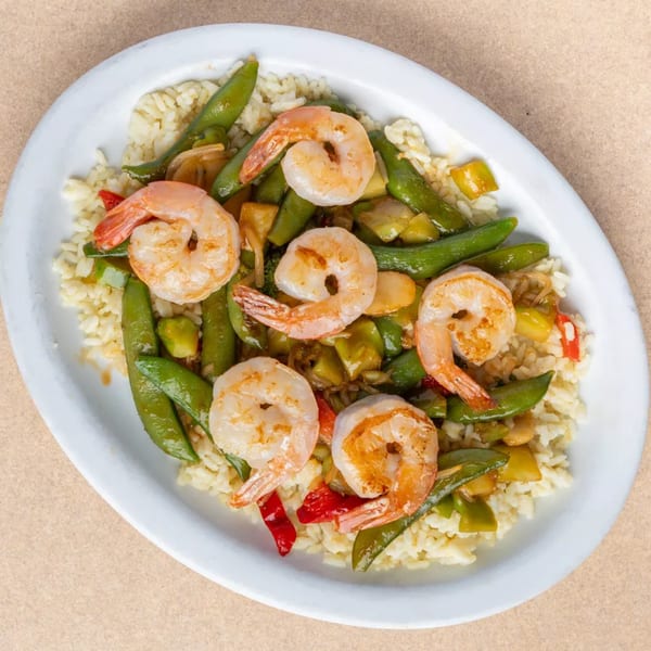 Shrimp stir-fry with snap peas, bell peppers, and rice on a white oval plate.