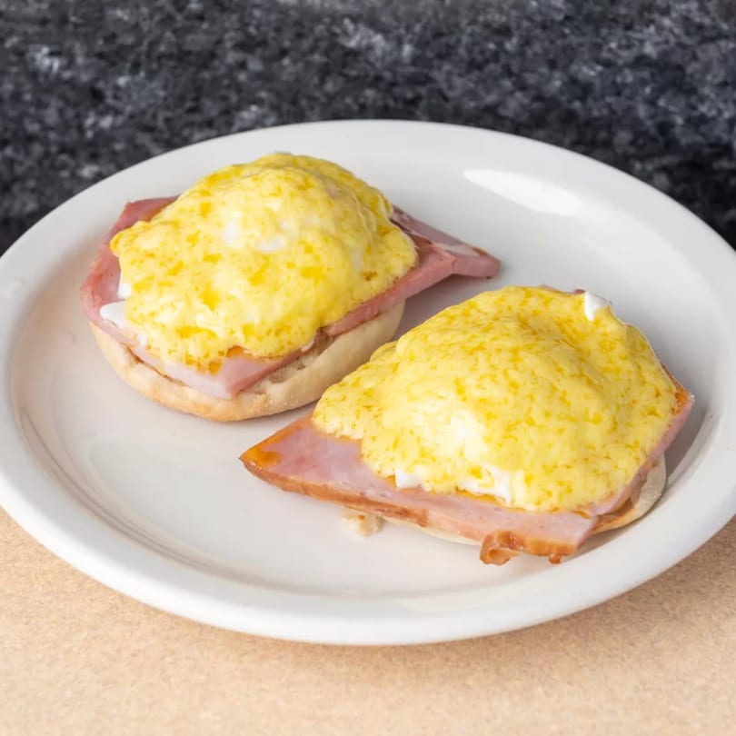 Two servings of Eggs Benedict with ham and hollandaise sauce on a white plate.
