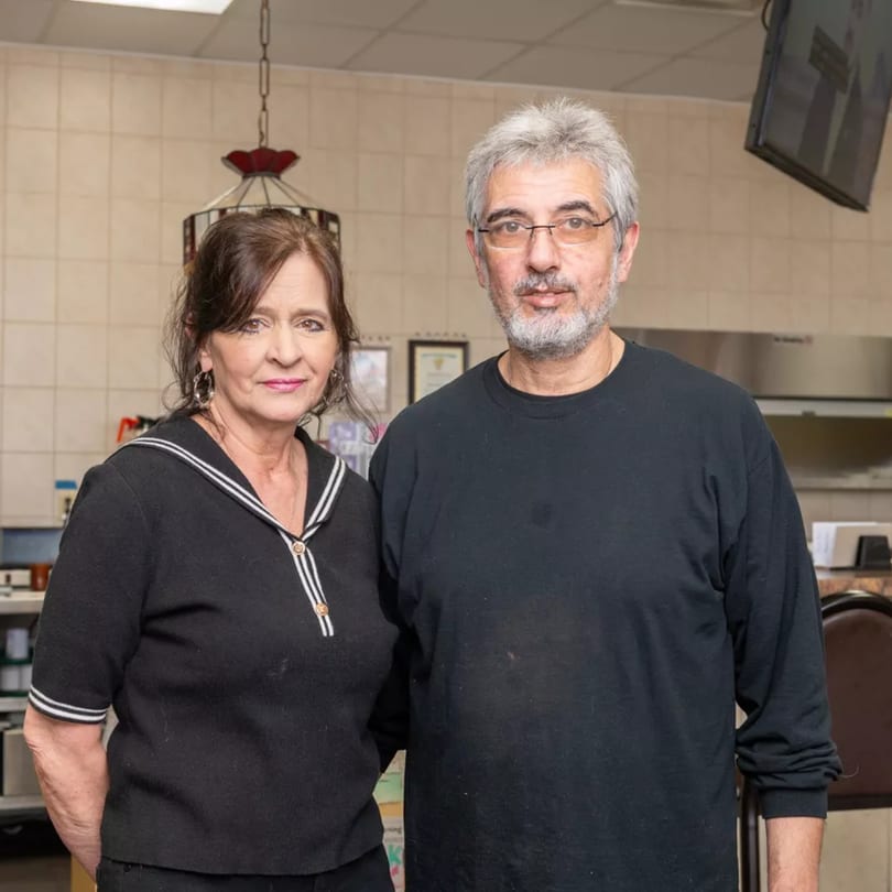 Two owners, a woman and a man, standing side-by-side in their American diner.