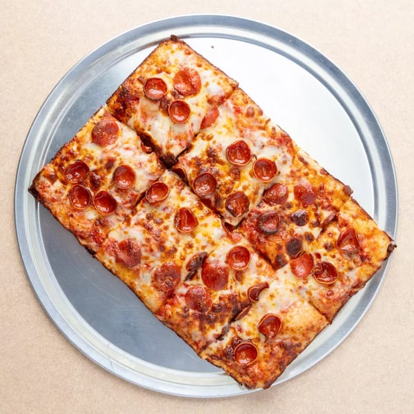 Square pepperoni pizza, cut into eight slices, on a round metal tray.
