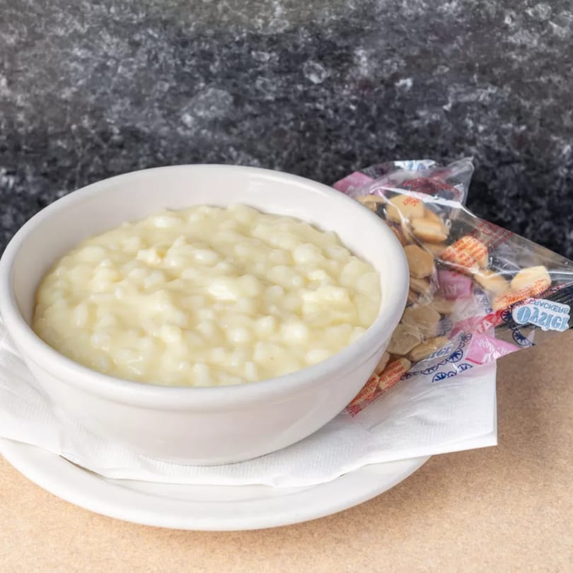 Creamy rice pudding in a white bowl with a side of oyster crackers on a white plate.