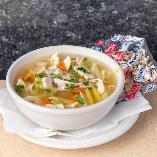 Chicken noodle soup with carrots, celery, and parsley in a white bowl with oyster crackers.