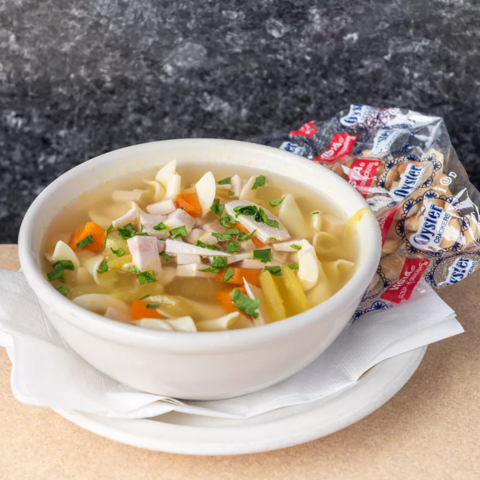 Chicken noodle soup with carrots, celery, and parsley in a white bowl with oyster crackers.